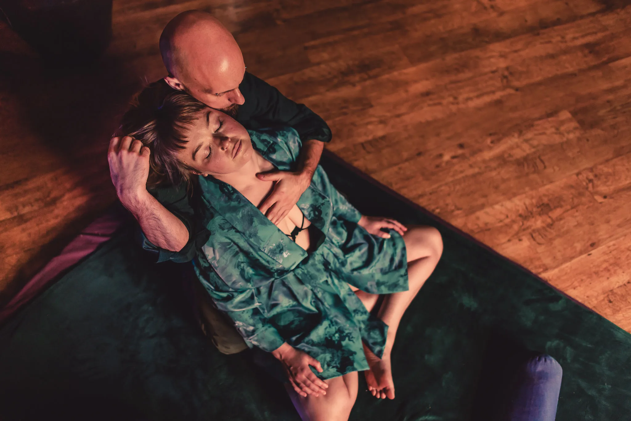 Ben holding a client in a green robe, her head resting against him, on a wooden floor